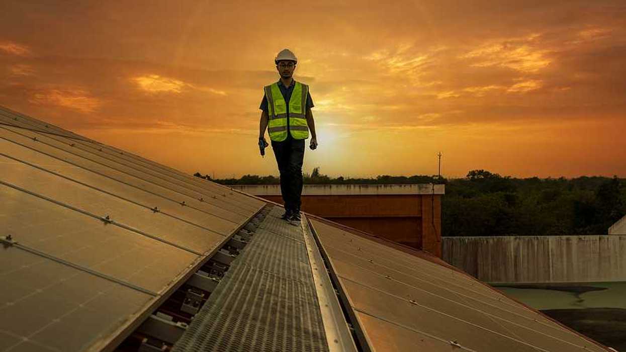 A maintenance worker walking along a solar panel with the sun in the background