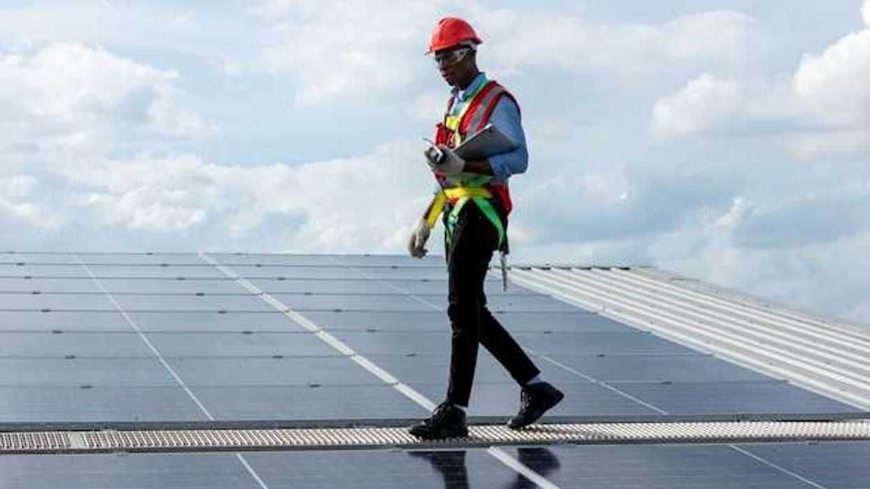 A maintenance worker walking alongside solar panels on a roof