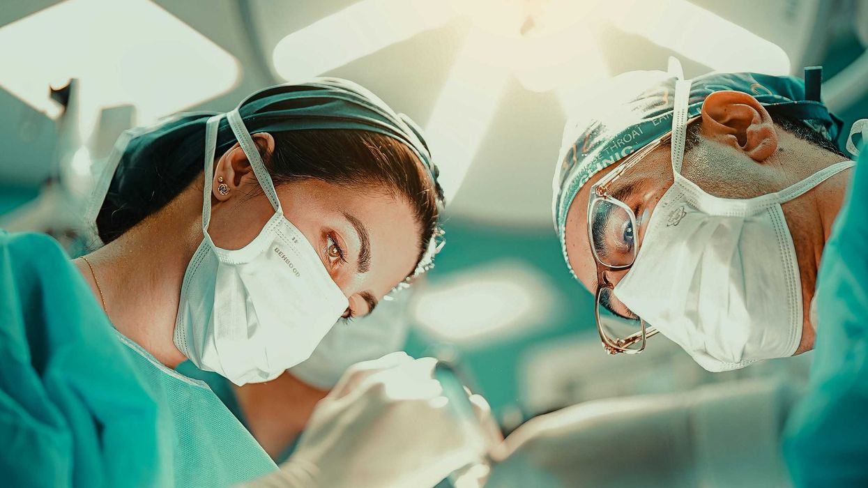 A male and female surgeon in green scrubs and masks looking down.