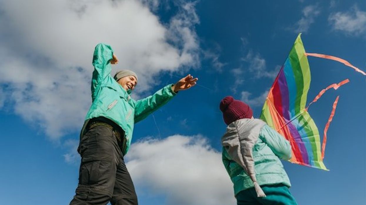 A man and a child flying a kite with white clouds in a blue sky