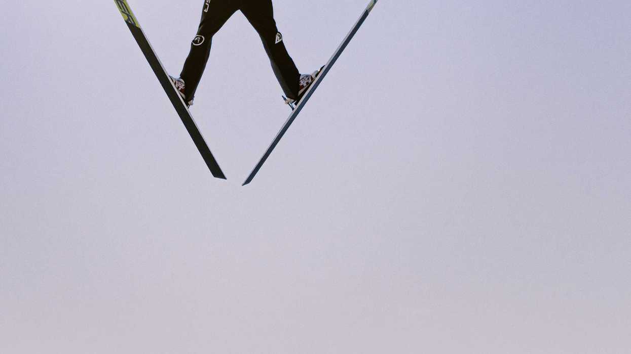 a man flying through the air on skis with sun in background.