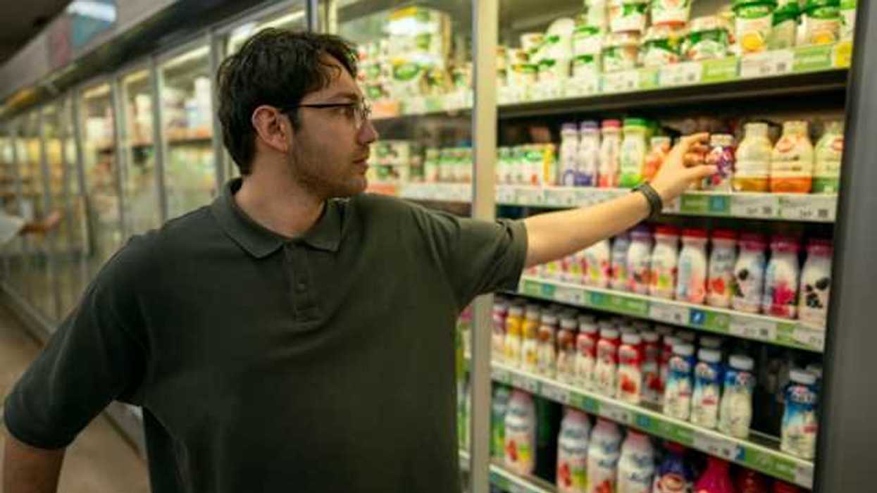 A man grabbing a plastic container of yogurt from a grocery store refrigerator