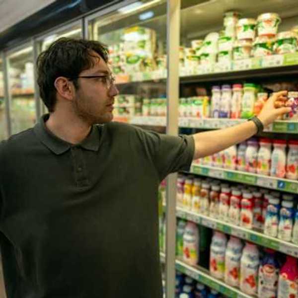 A man grabbing a plastic container of yogurt from a grocery store refrigerator