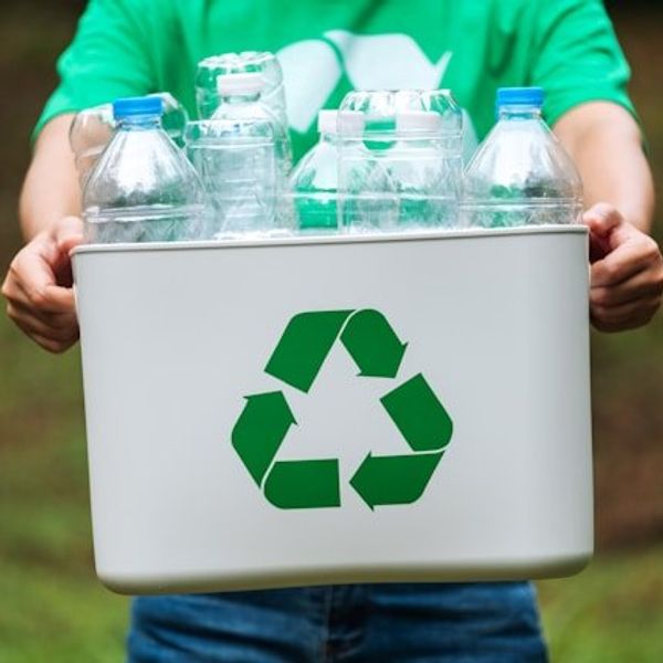 A man holding a recycling bucket filled with plastic bottles.