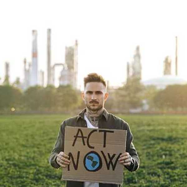 A man holding a sign saying 'Act Now' with a power plant in the background