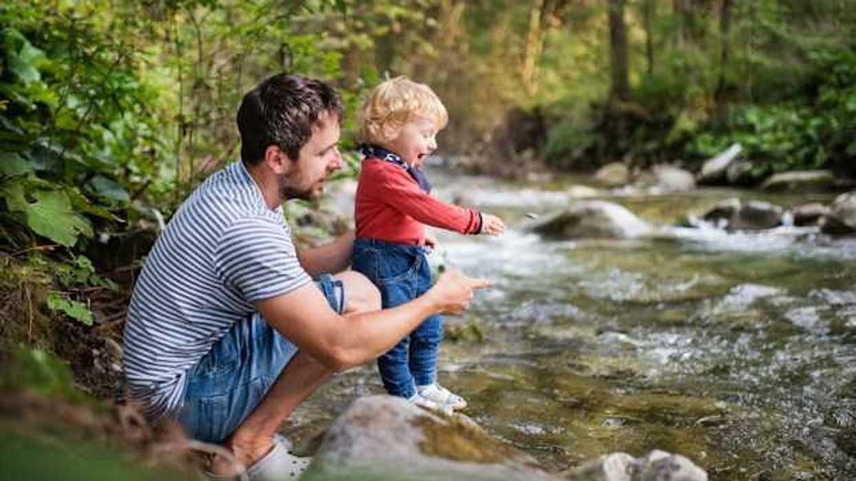 A man holding his toddler why they explore a creek
