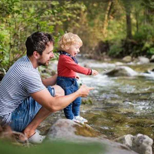 A man holding his toddler why they explore a creek