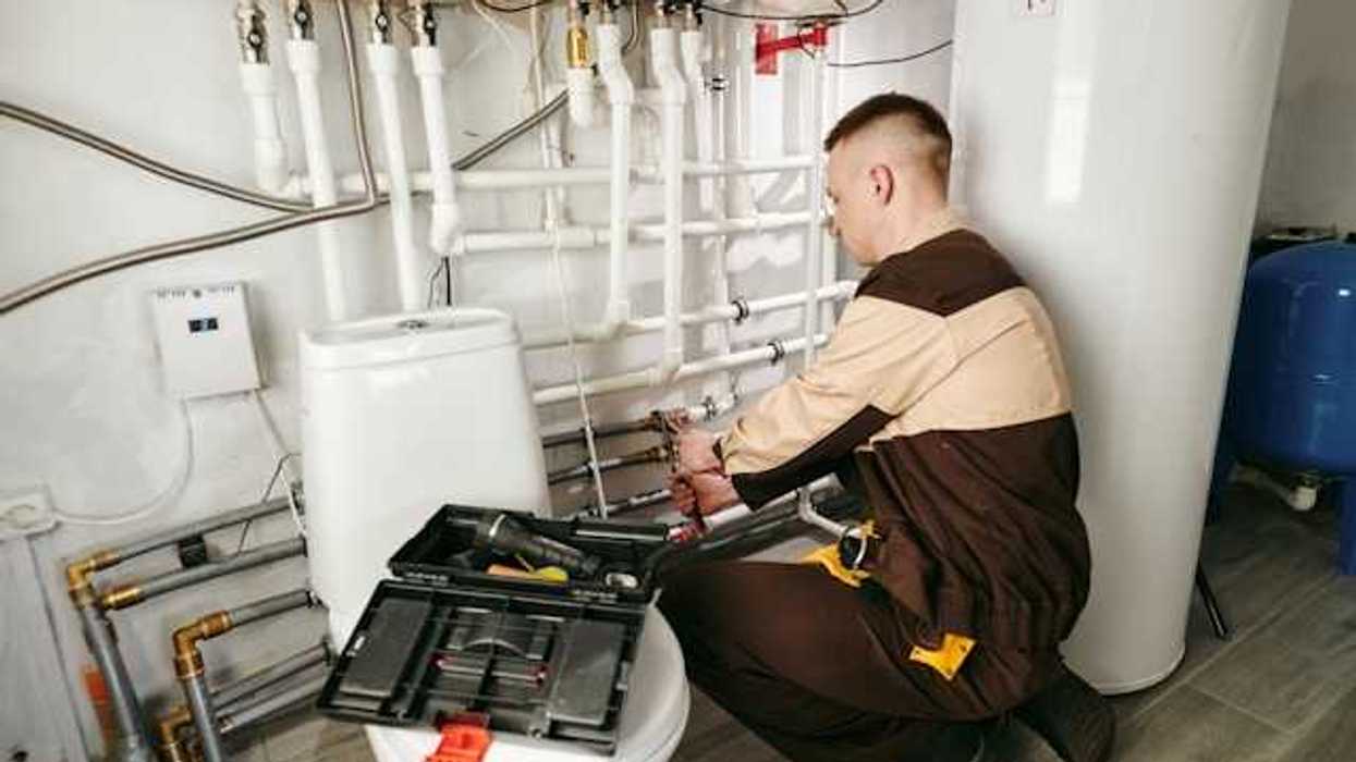 A man in a brown uniform with a tool box working on a heating system