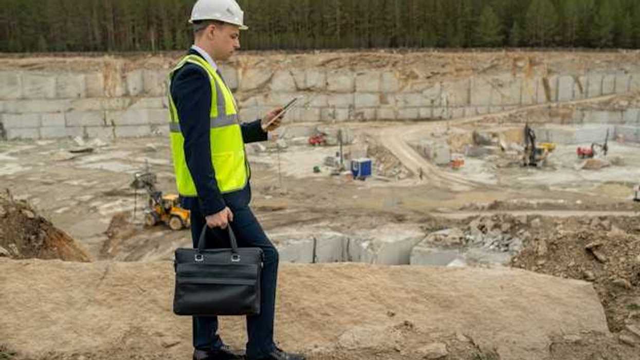 A man in a suit wearing a hard hat and a yellow vest at the edge of a pit