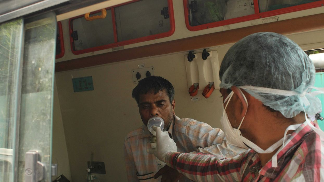 a man in a surgical mask putting a respiratory mask on a man in a hospital room.
