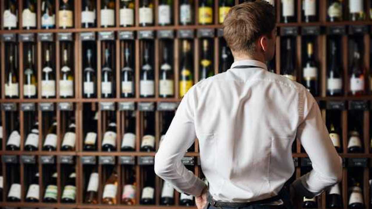 A man in a white shirt looking at a wall of wine bottles