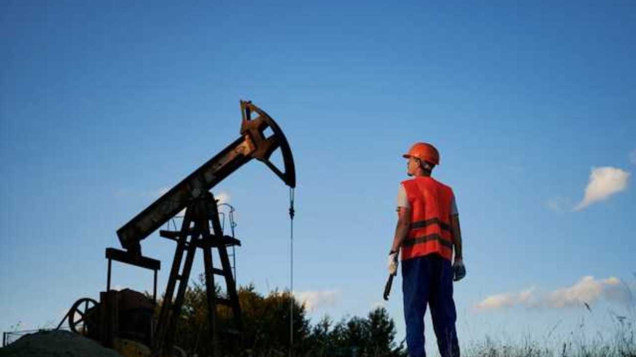 A man in an orange vest looking up at an oil pump jack