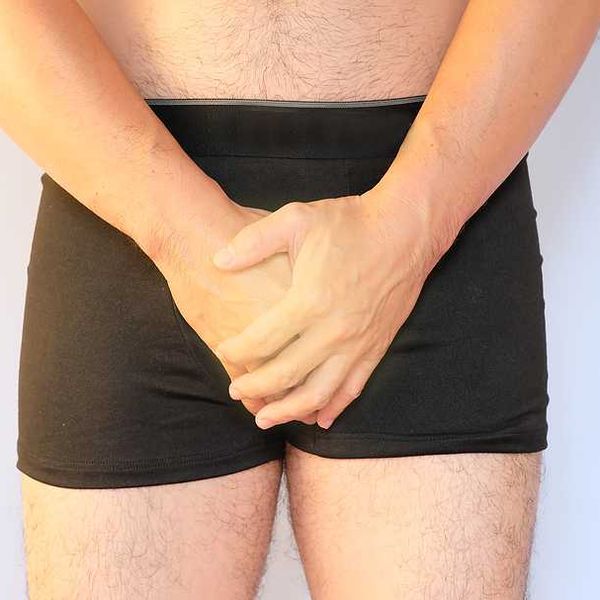 A man in briefs holding his hands over his genital area