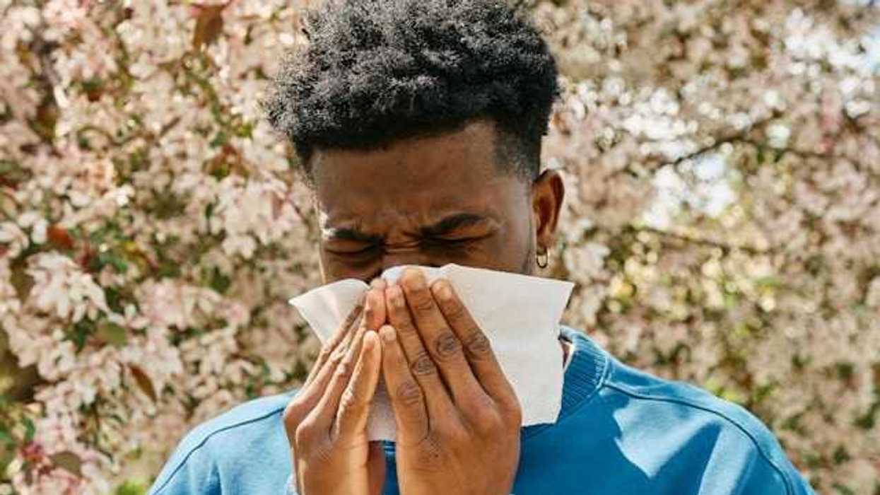 A man in front of a flowering tree blowing his nose