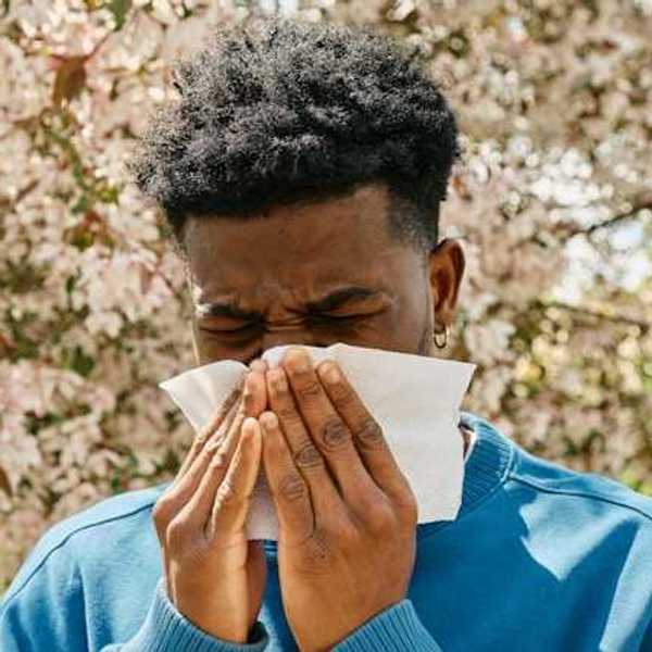 A man in front of a flowering tree blowing his nose