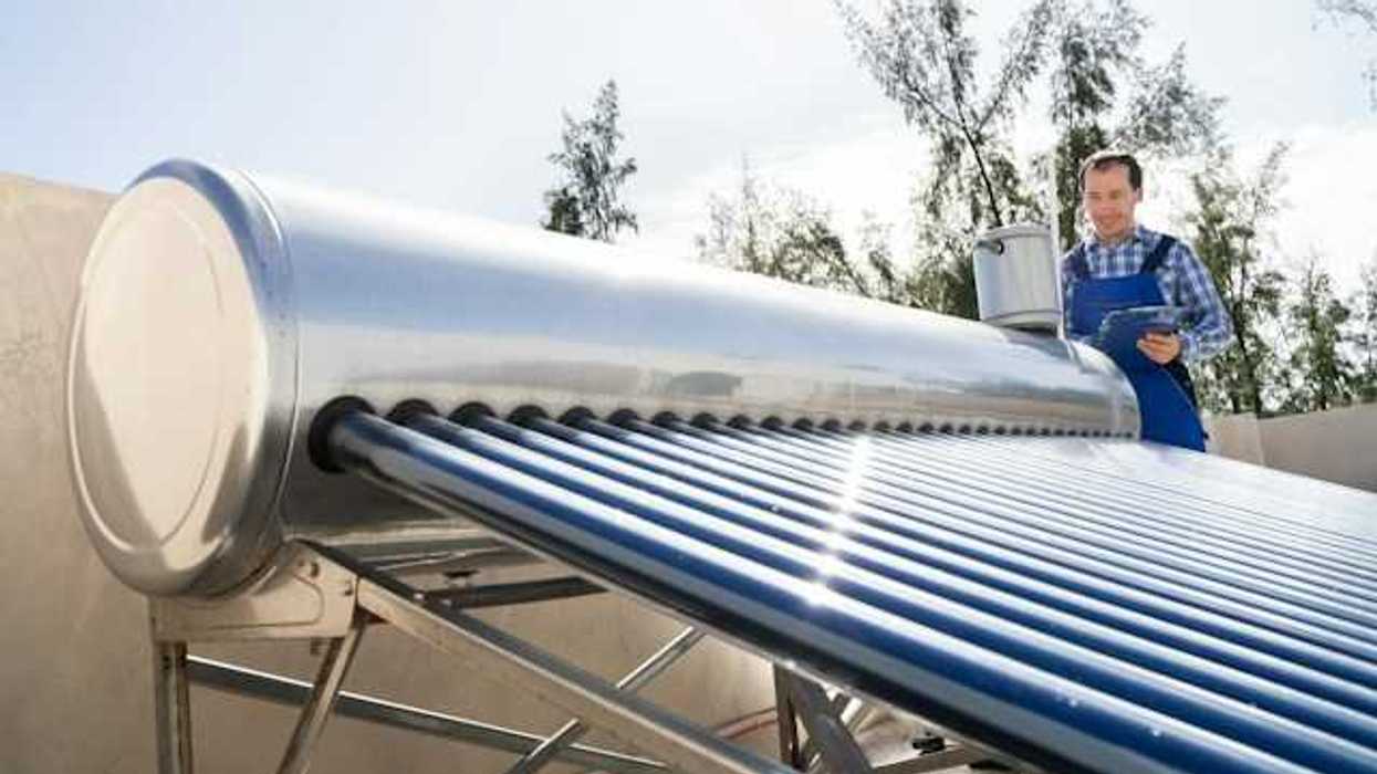 A man inspects a solar water heater on a roof