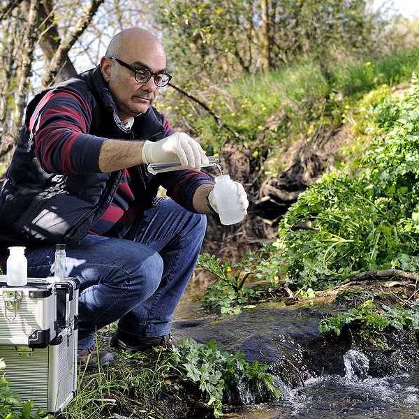 A man kneeling by a stream taking a water sample
