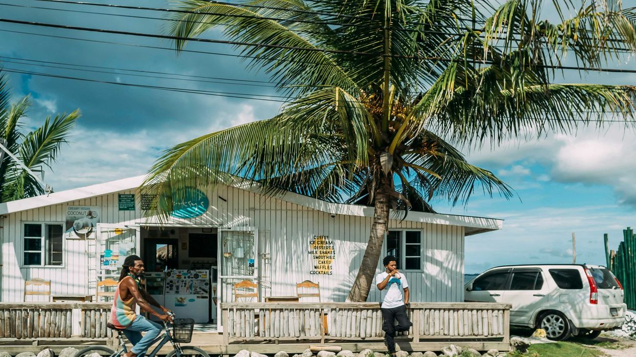 A man of African descent wearing a tank top riding bicycle in front of white building near palm tree during daytime.