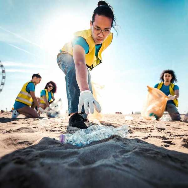 A man reaches for a discarded plastic bottle as 5 people wearing yellow vests pick up beach litter