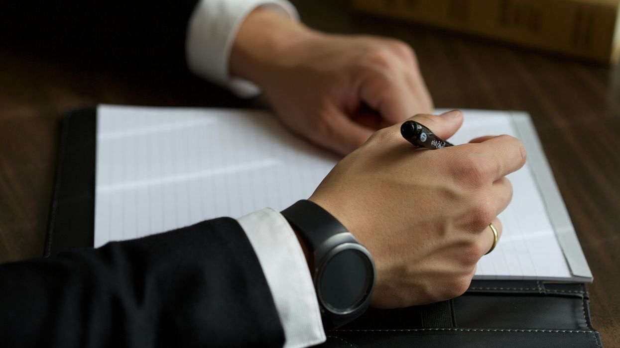A man's hands with a pen writing on a pad of paper.