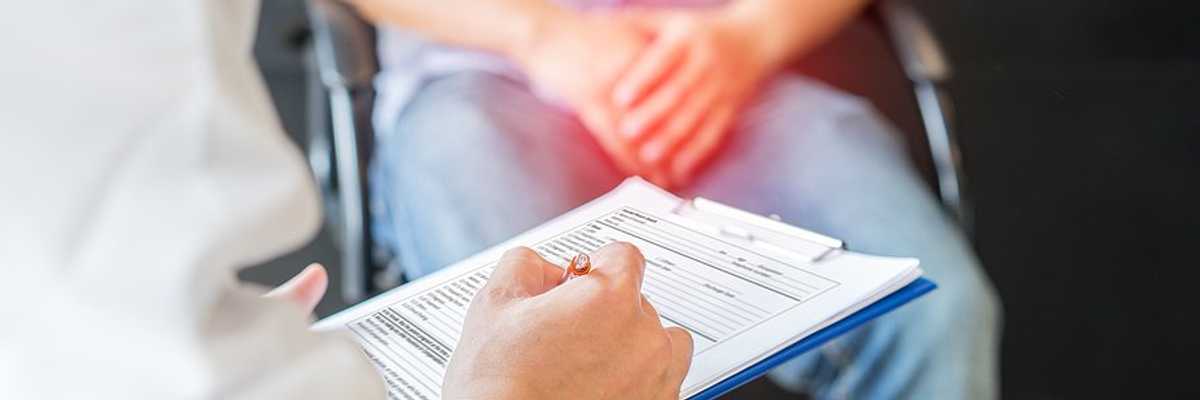 A man sitting in a chair with his hands resting over his groin talking to a doctor.