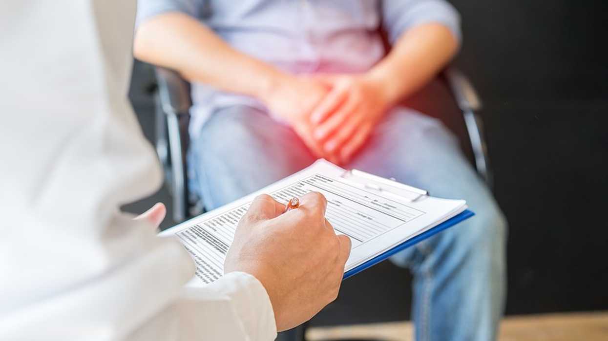 A man sitting in a chair with his hands resting over his groin talking to a doctor.
