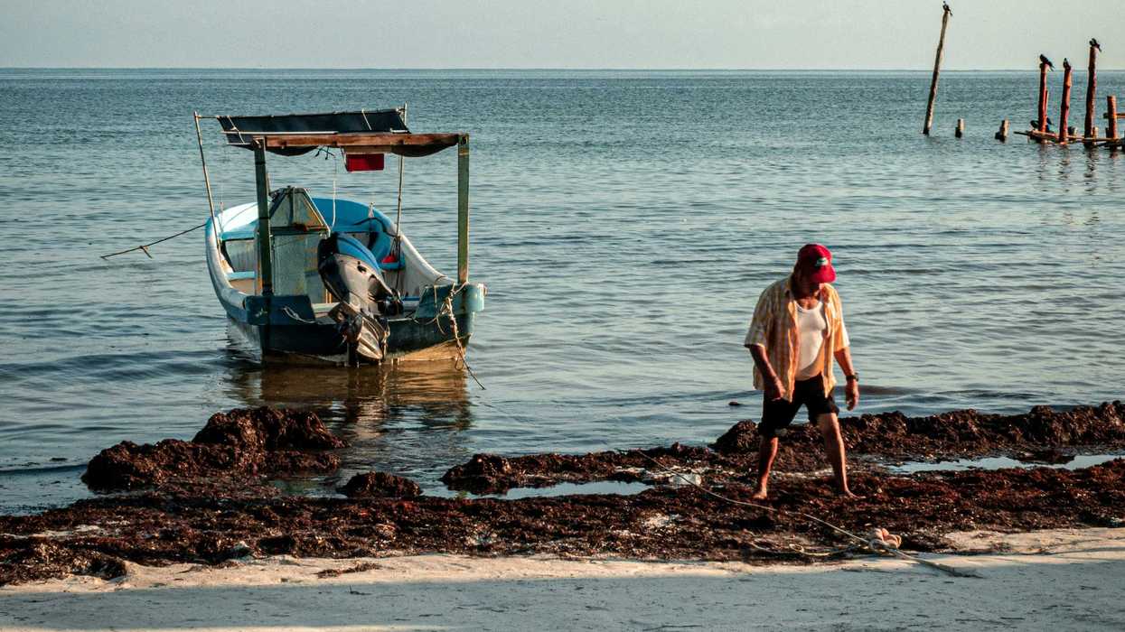 a man sitting on the shore of a beach next to a boat.