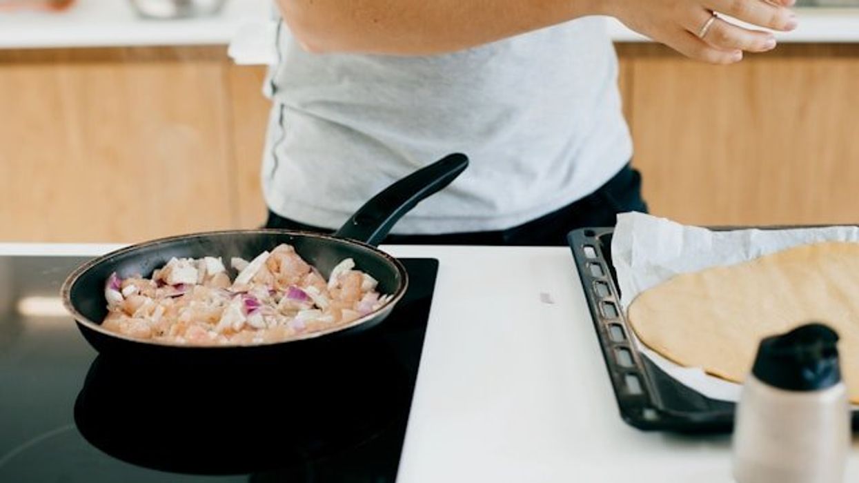 A man standing at a stove with a nonstick pan filled with chicken