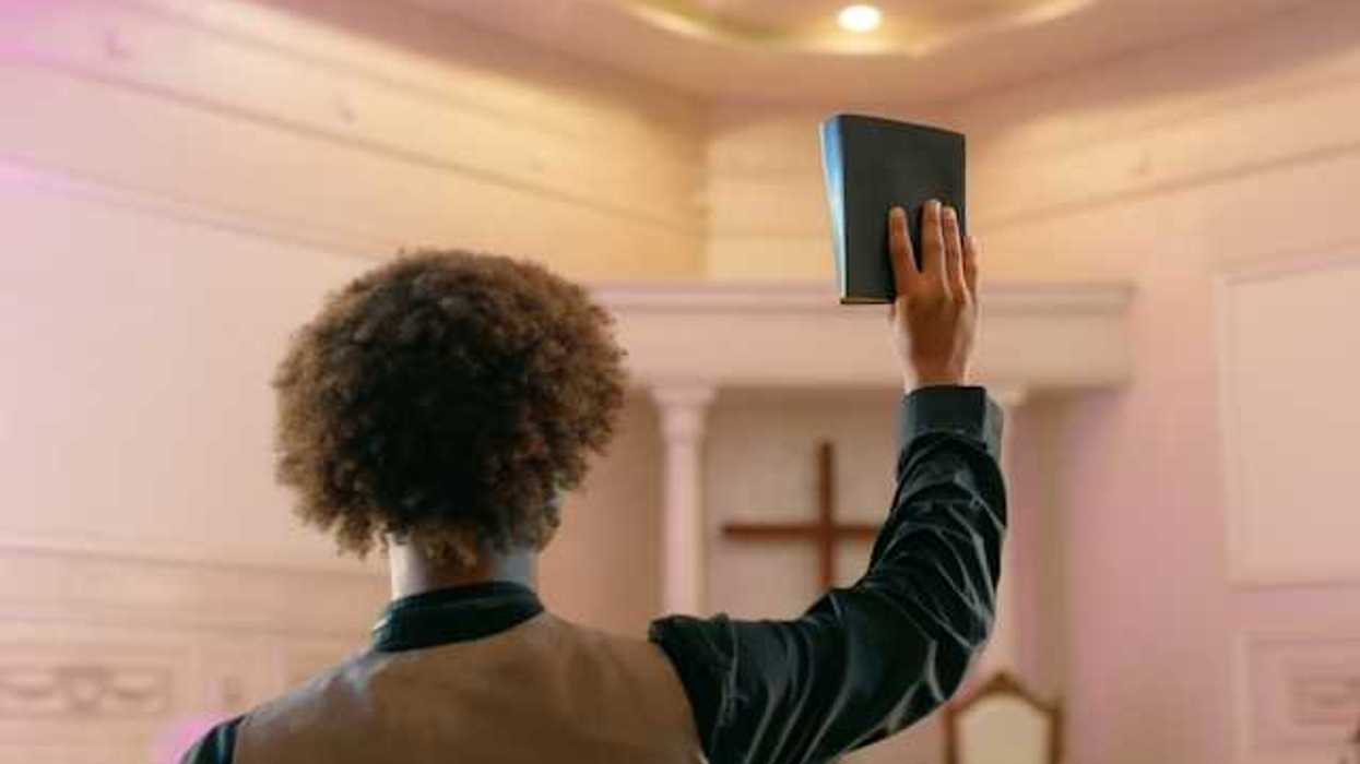 A man standing facing a Christian cross with a book raised in his right hand