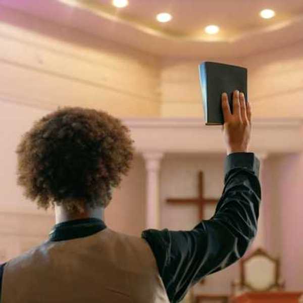 A man standing facing a Christian cross with a book raised in his right hand