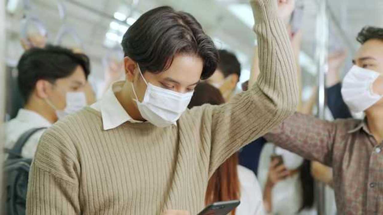 A man standing in a crowded subway train wearing a face mask