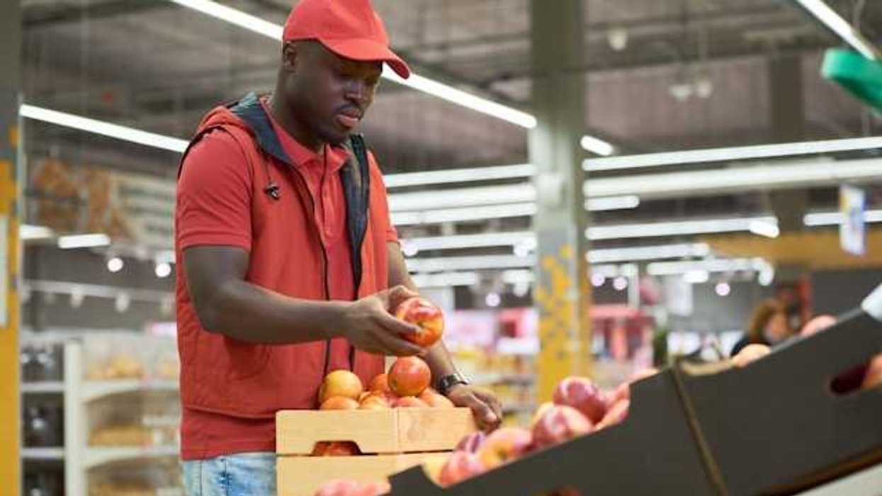 A man standing in front of a fruit display in a grocery store looking at peaches