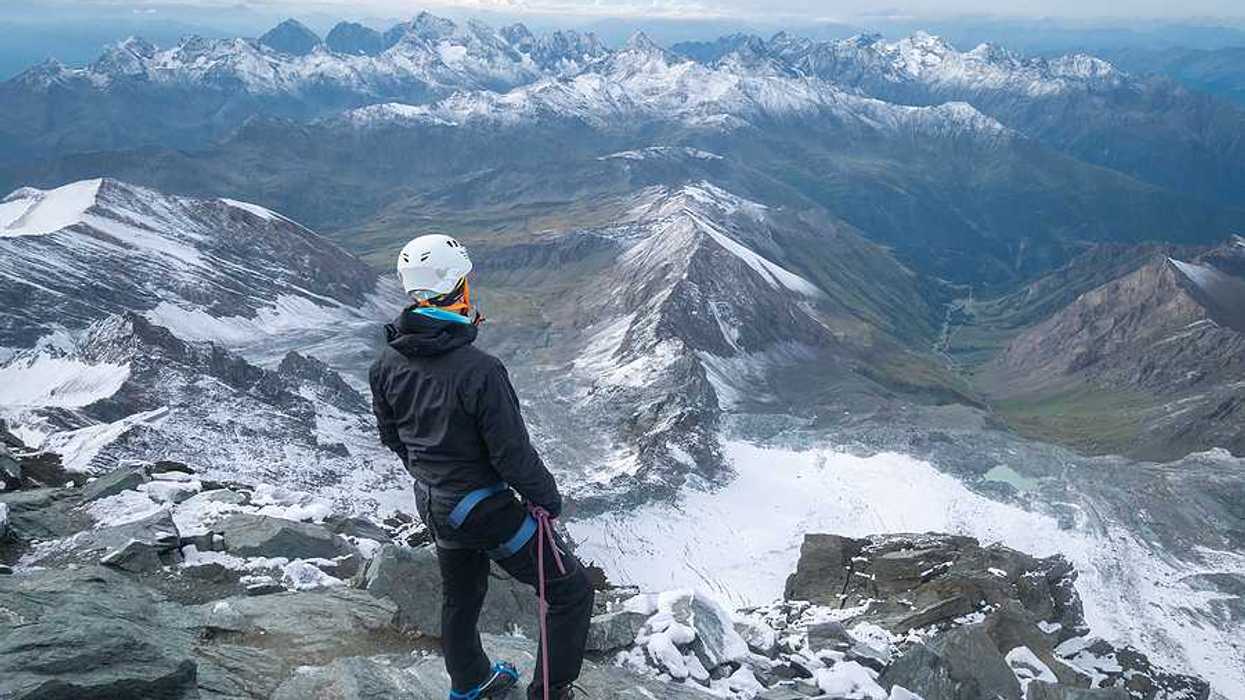 A man standing on a peak looking out over a snowy mountainous landscape
