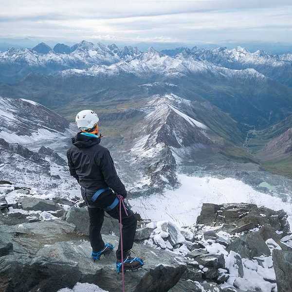 A man standing on a peak looking out over a snowy mountainous landscape