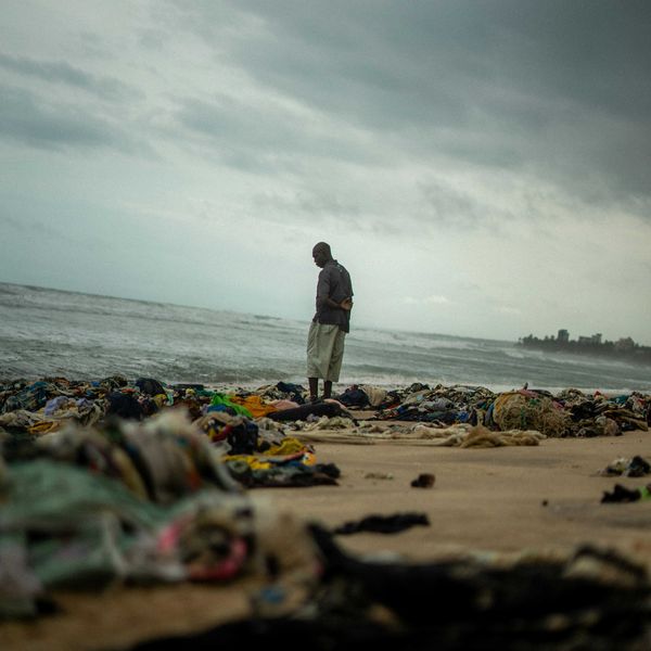 a man standing on top of a sandy beach next to the ocean with piles of trash surrounding him.