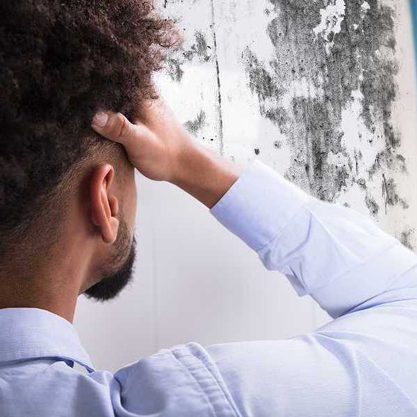 A man standing with his hand to his forehead looking at a wall with a black substance on it