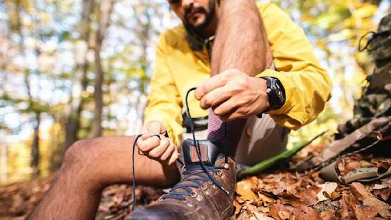 A man tying his hiking shoes while sitting in a forest