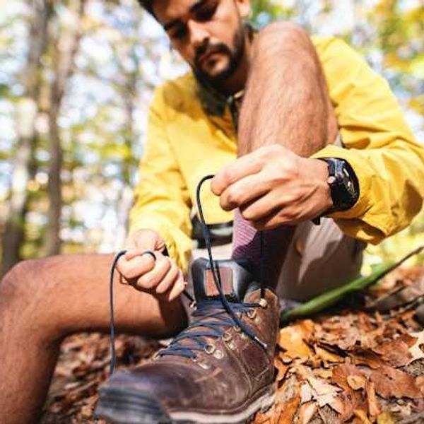 A man tying his hiking shoes while sitting in a forest