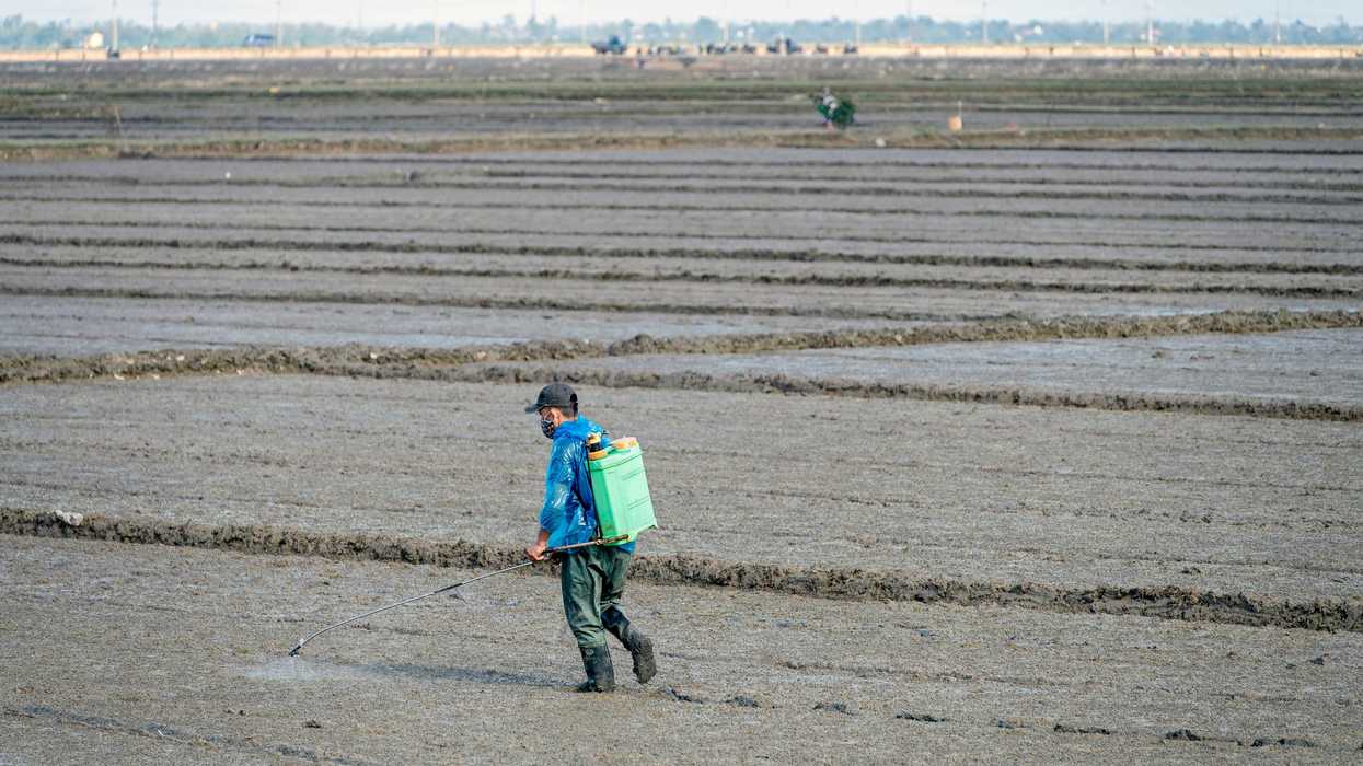 a man walking across a field carrying a fumigation backpack device.