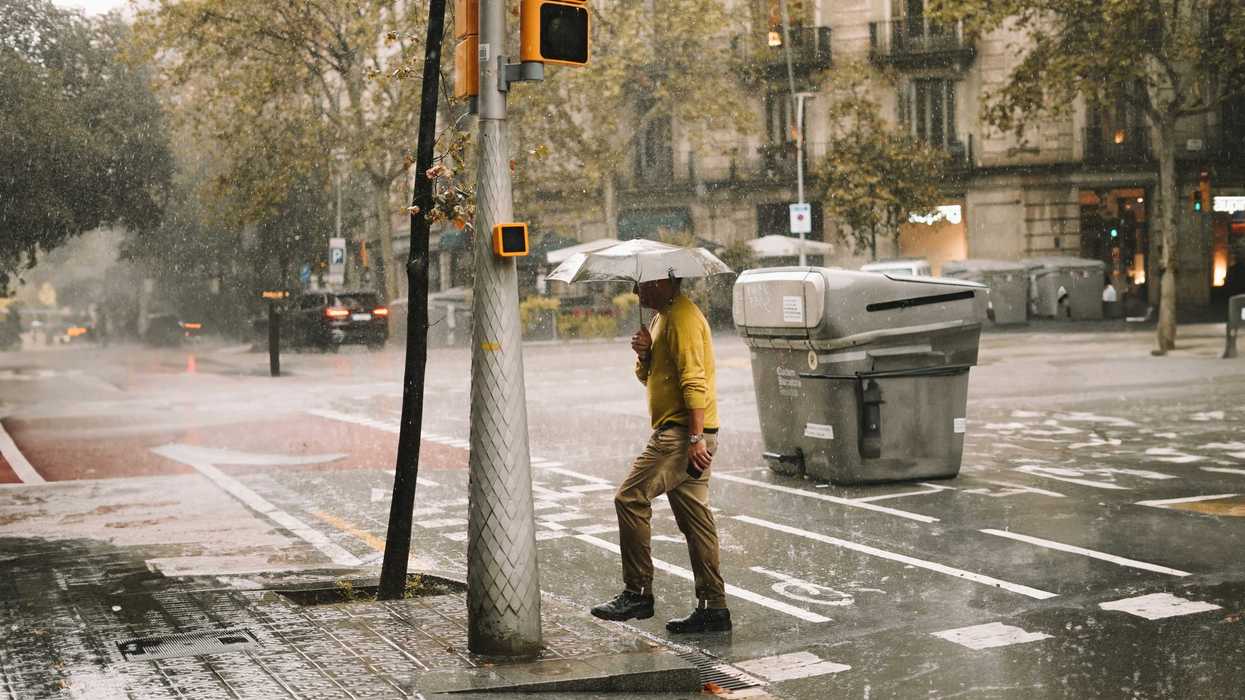 A man walking down a Barcleona street holding an umbrella in the rain.