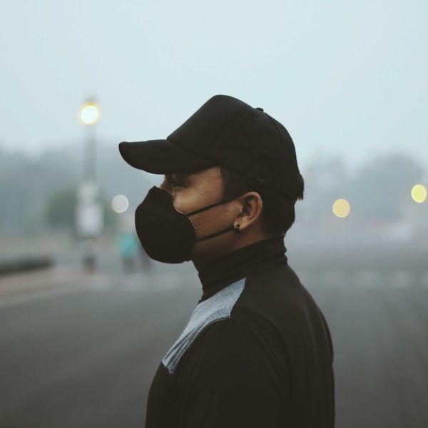 a man wearing a black hat and a black face mask with a polluted background