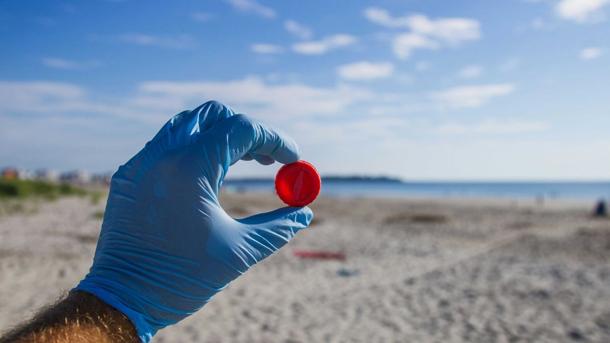 A man wearing a blue glove holding a plastic bottle cap on a beach