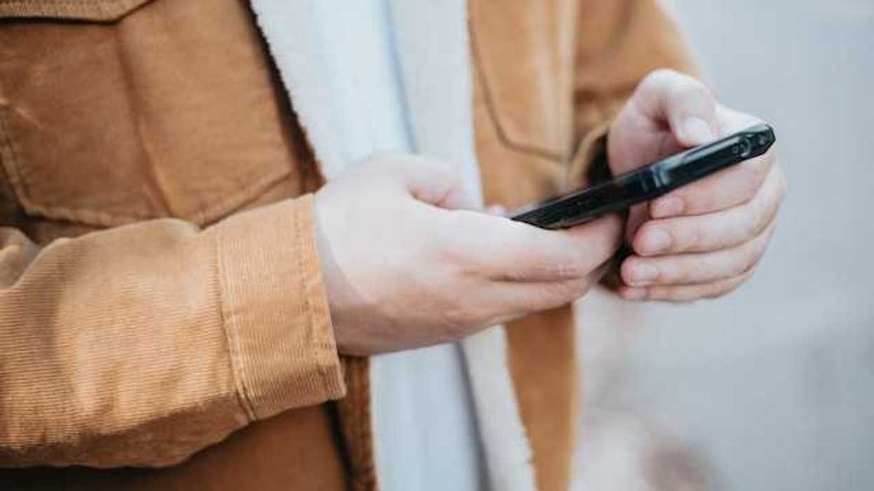 A man wearing a brown coat with his cell phone in his hands