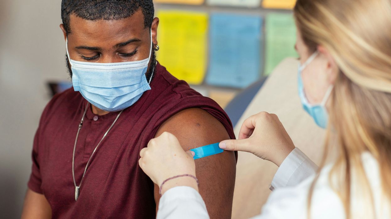 A man wearing a face mask has a band aid placed on his arm after having a vaccine shot.