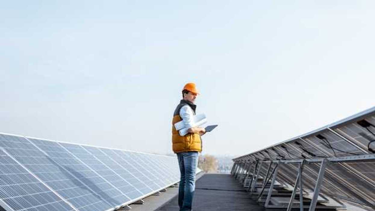 A man wearing a hardhat on a roof inspecting solar panels
