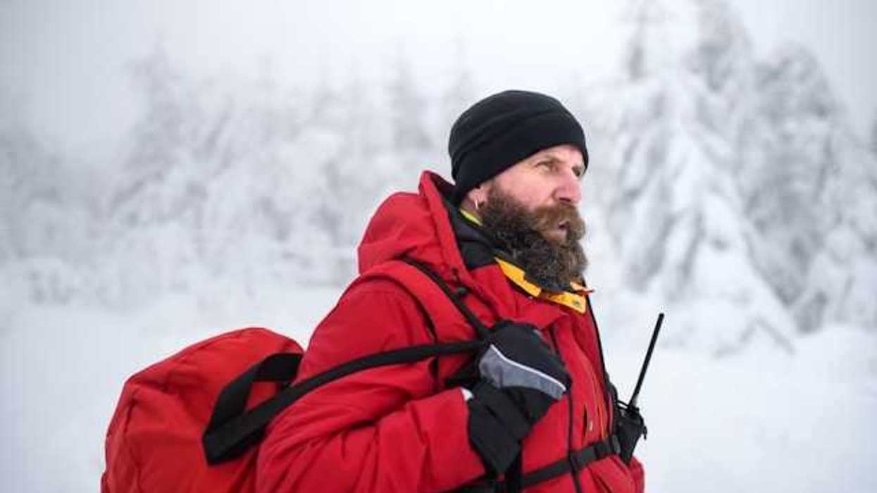 A man wearing a red jacket and carrying a red bag walking through a snowy landscape