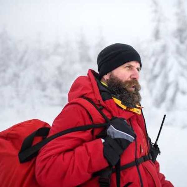 A man wearing a red jacket and carrying a red bag walking through a snowy landscape