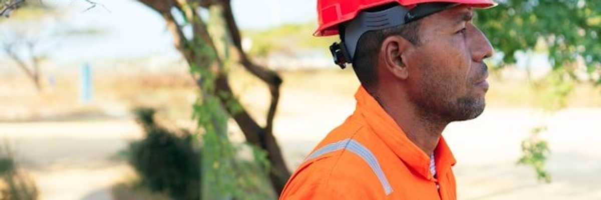 A man wearing an orange safety jumpsuit and hardhat on a sunny day.