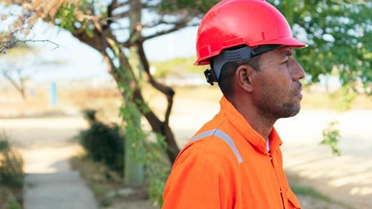 A man wearing an orange safety jumpsuit and hardhat on a sunny day.