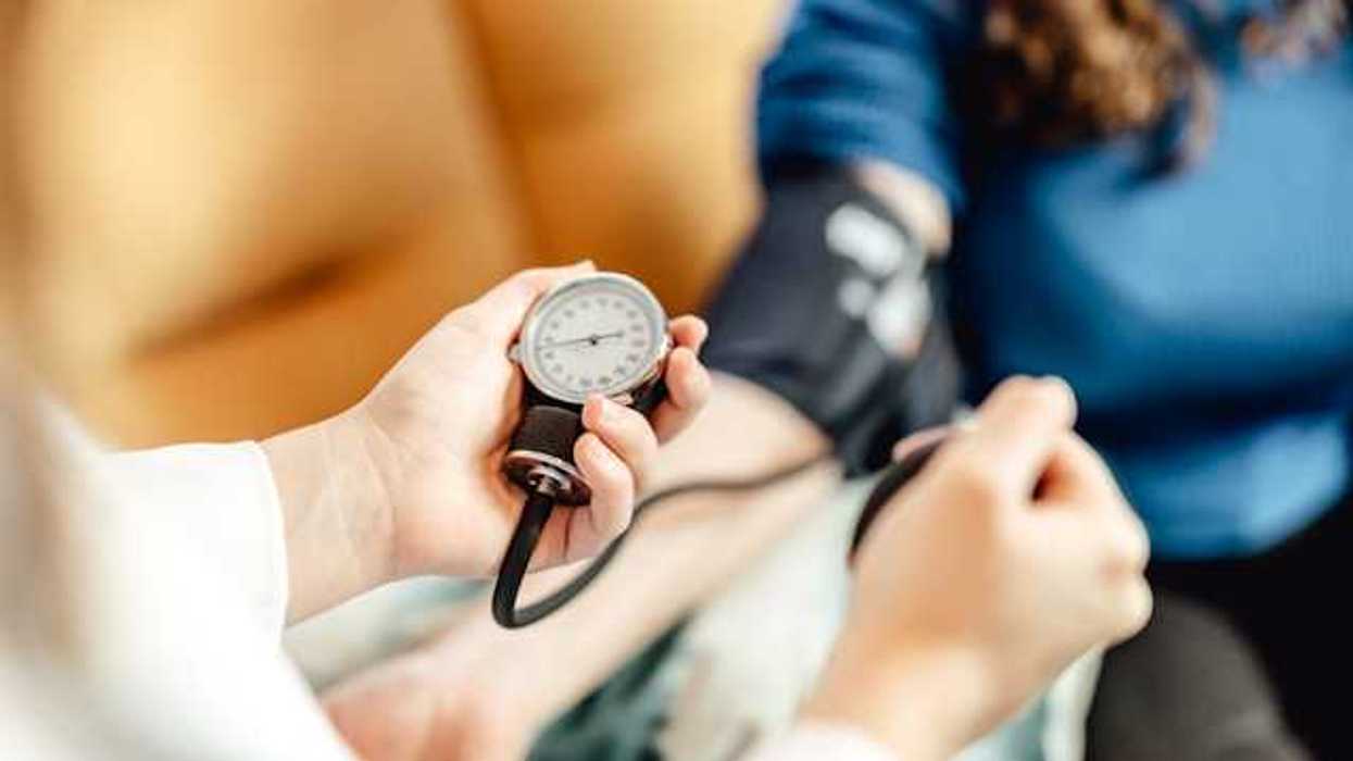 A medical professional taking the blood pressure of a woman sitting in a chair